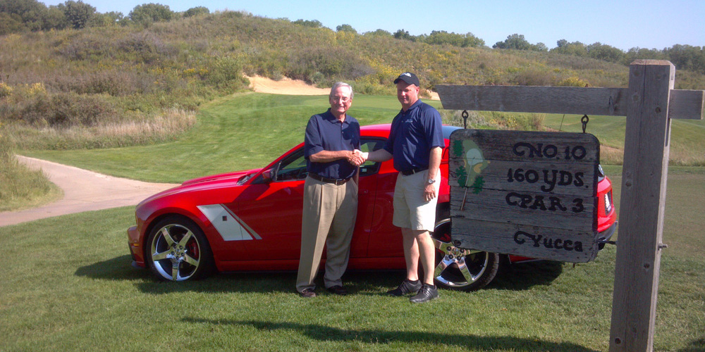 photo - Tom West (left) shakes hands with Phil Nightingale, general manager of Mel Hambleton Ford, as he receives his hole-in-one prize of a 2013 Roush Stage 3 Ford Mustang at the Hesston College Kansas Golf Benefit at Prairie Dunes Country Club in Hutchinson.