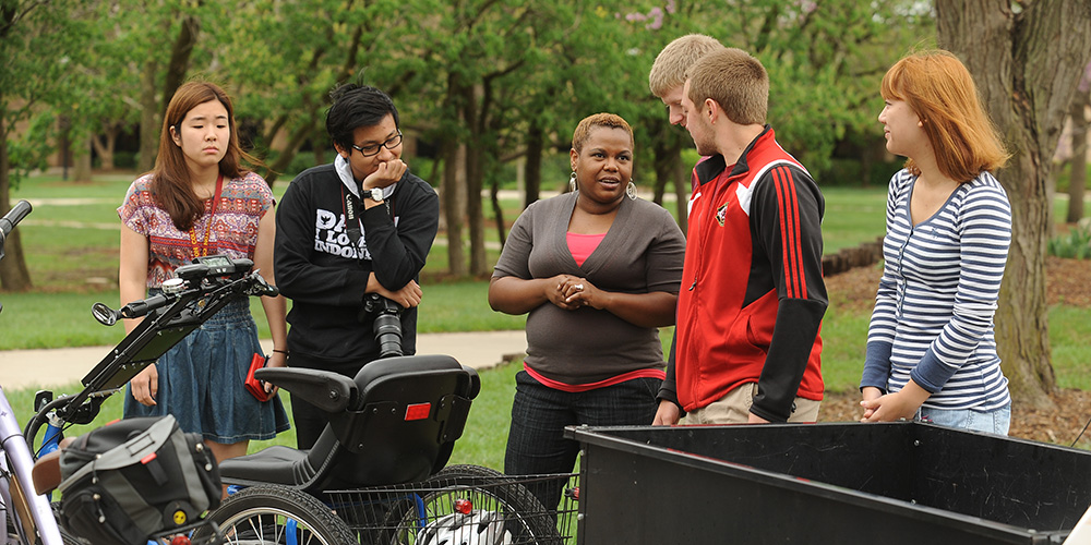 photo - Natural science instructor Marelby Mosquera (third from left) talks with a group of students about the solar-charged personal activities vehicle built by students in the college’s Physics II course.
