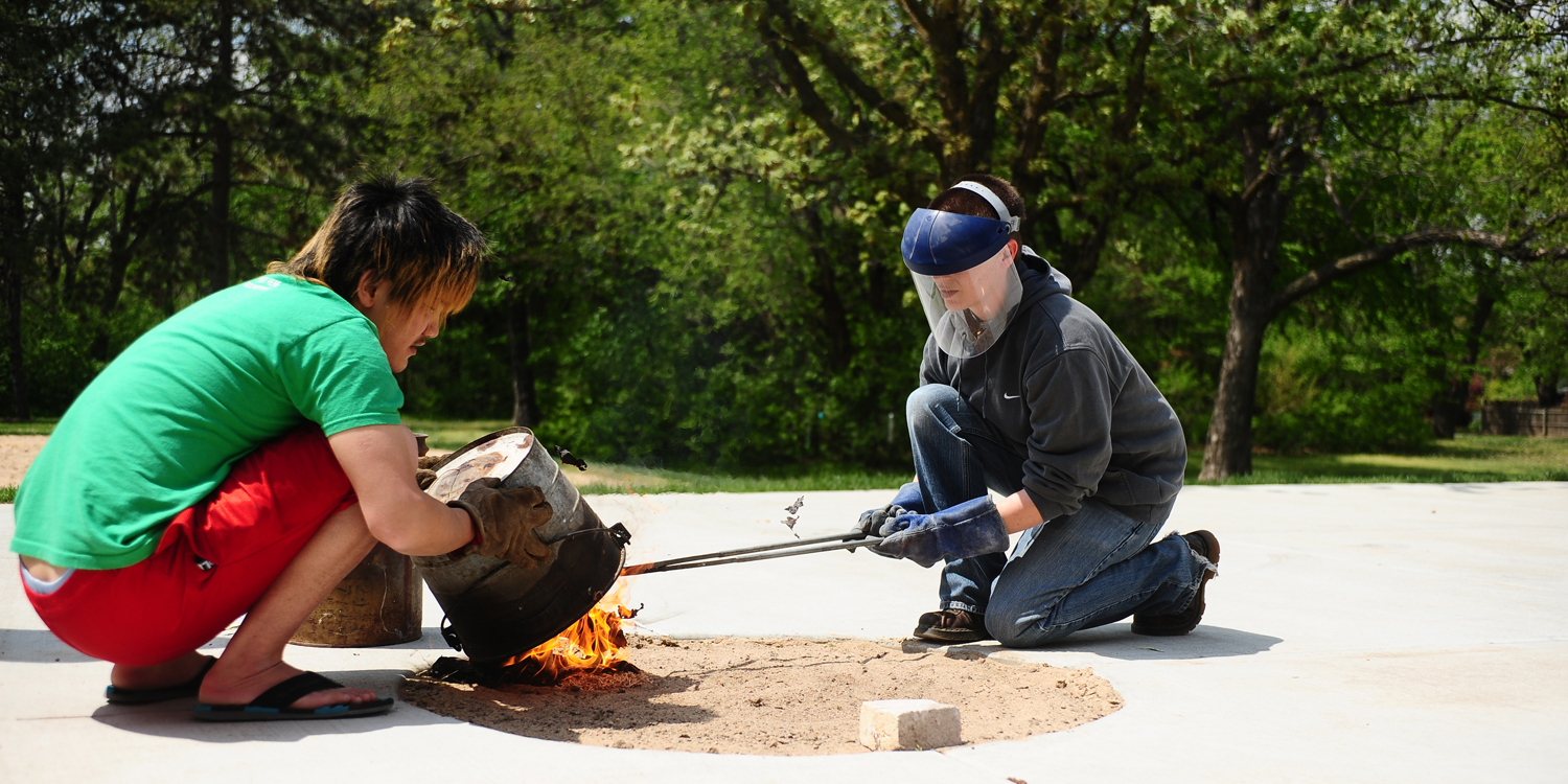 photo - Hesston College ceramics instructor Hanna Eastin (right) and a student work on a raku firing of ceramics pieces.