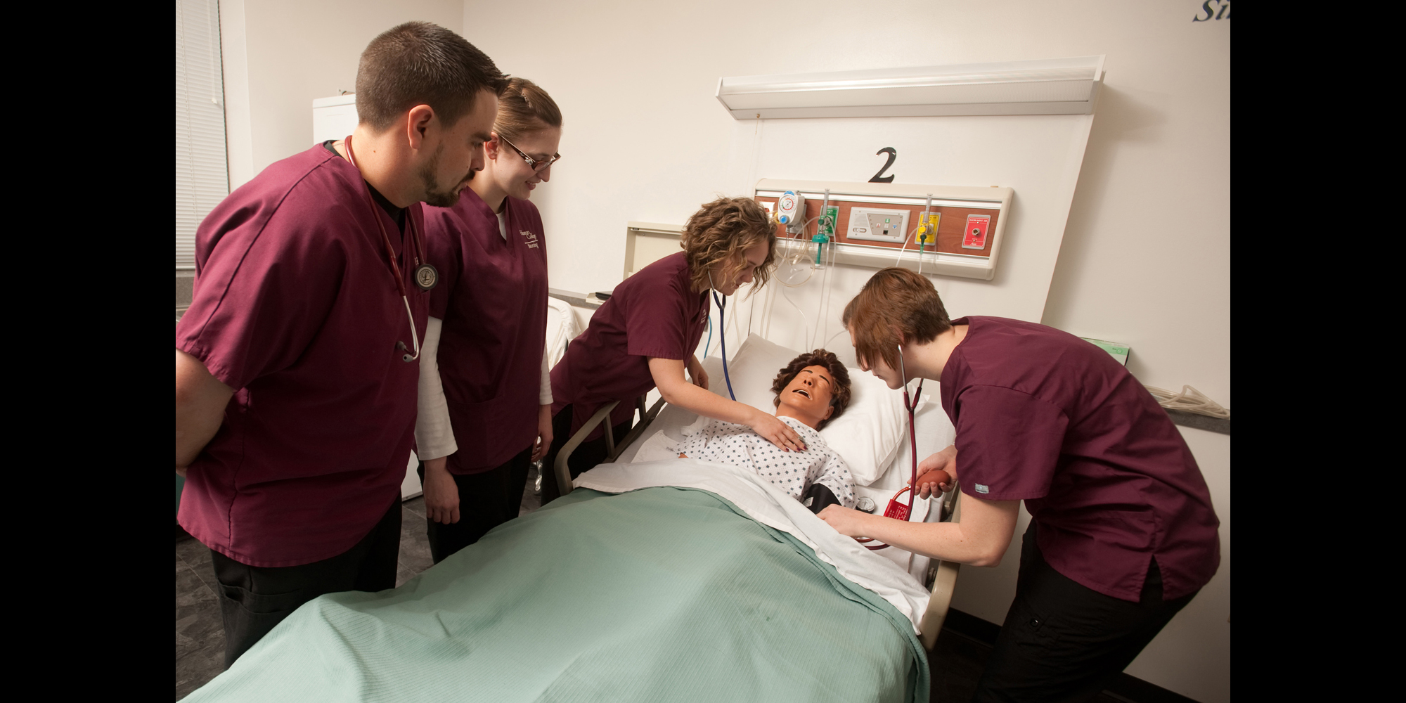 photo - Hesston College Nursing students Chad Jones (Halstead, Kan.), Jennifer Kaberline (McPherson, Kan.), Brianne Stutzman (Hesston, Kan.) and Rinda Amstutz (Goessel, Kan.) practice on a sim patient in an on-campus nursing lab.