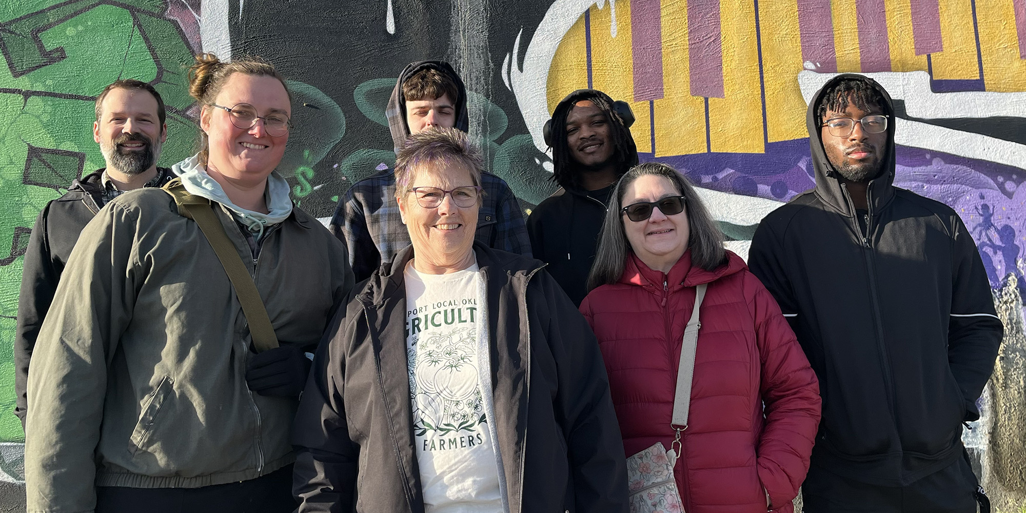 photo - Hesston College students pose in front of the Black Wall Street mural in Tulsa’s Greenwood District during their Urban Life and Culture spring break trip, where they learned about the history, resilience and ongoing legacy of the Greenwood community. Back row: Peter Lehman, Jacob Buller, Jaden Watson, Justin Young. Front row: Lilith Jackson, Margaret Brewer, Priscilla Spiker