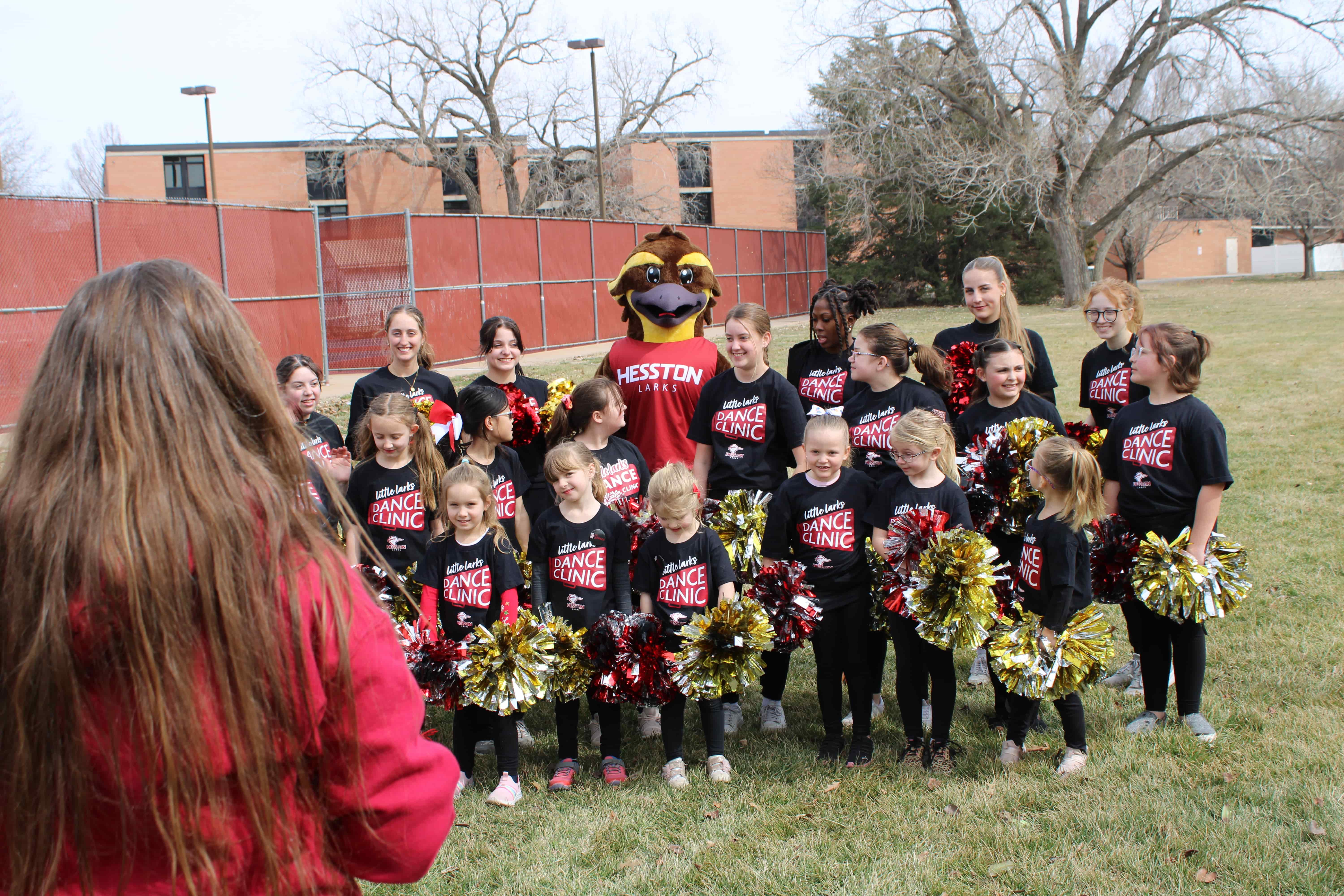 Young group of school-aged cheerleaders pose with pom-poms and the Lark mascot.