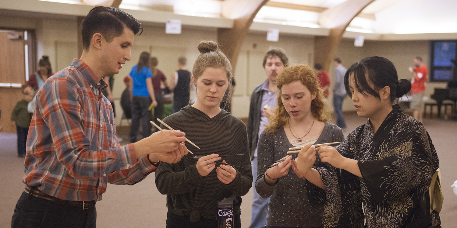 photo - Hesston College sophomore Kaho Yanagidaira (Chino-shi, Japan) (right) and English faculty member Donovan Tann (left) give a lesson on using chopsticks to sophomores Morgan Leavy (Telford, Pa.) and Emily Griffioen (Belmond, Iowa) at the college’s annual Culture’s Fair Oct. 10. After learning to use chopsticks, participants test their new skills by moving peas from one bowl to another. The Culture’s Fair is a chance for international students to share their customs, culture, music and food with the campus community. This fall, 39 international students representing 16 countries are part of the Hesston College community.