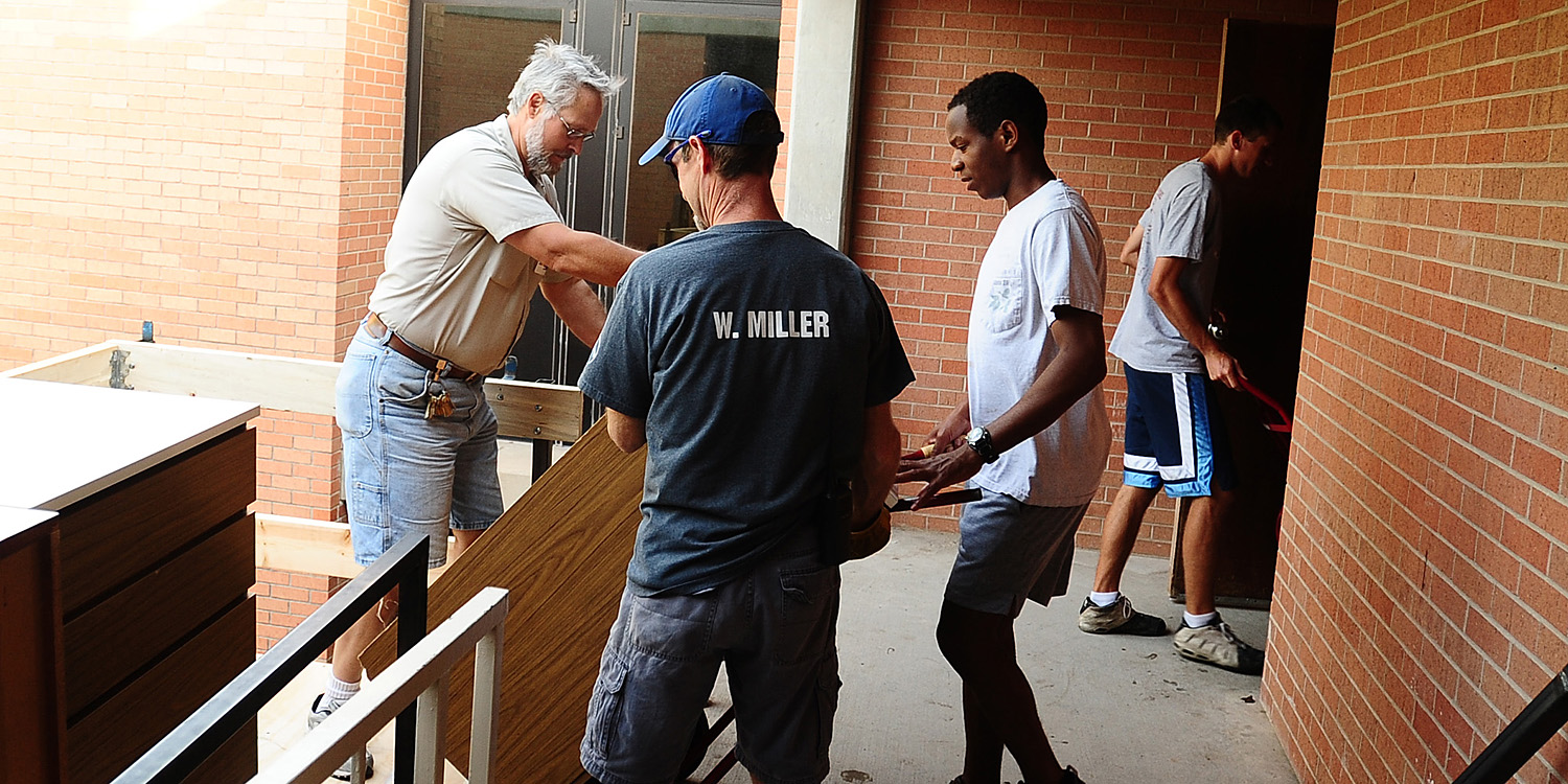 photo - Hesston College Facilities staff Tim Goering and Forrest Miller and student Curtis Denlinger of Perkasie, Pa. move dressers from Erb Hall central and west.