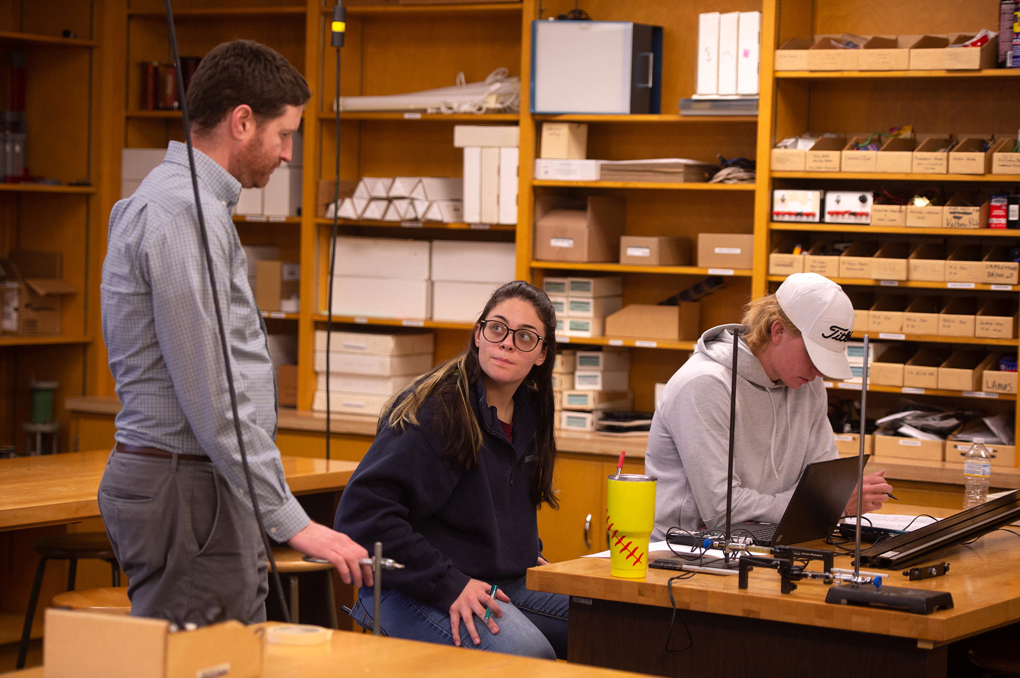 a professor answers questions as two students work on a physics lab assignment