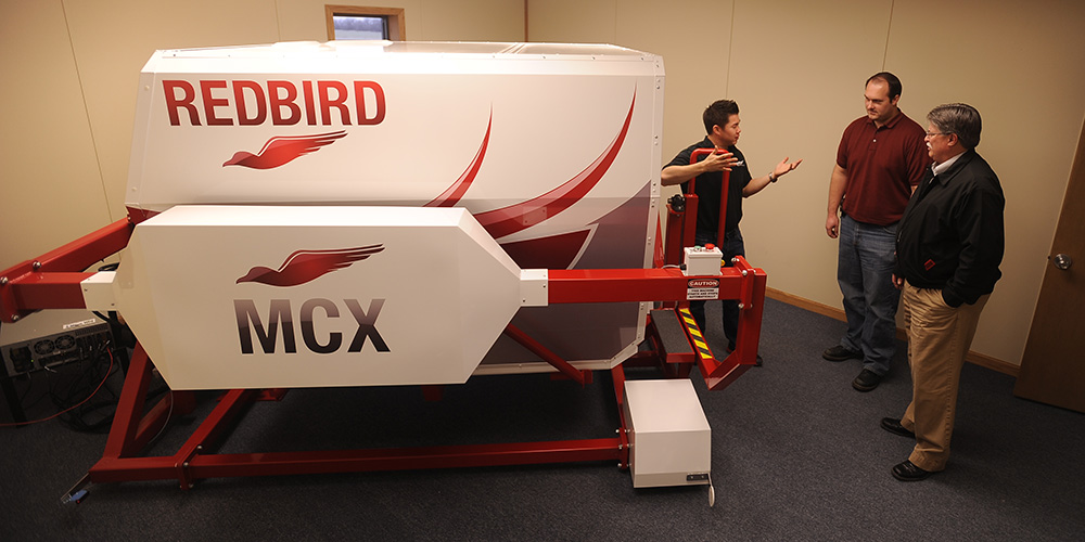 photo - Hesston College Aviation program director Dan Miller (right) and flight instructor Travis Pickerill (center) get maintenance tips about the college’s new Redbird MCX C182 G1000 GFC700 flight simulator.