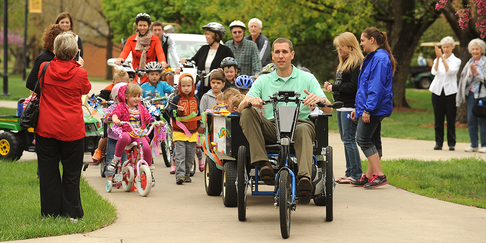 Mark Landes, Hesston College vice president of Finance and Auxiliary Services pulls a wagon of children from the college's preschool on a solar-charged personal activities vehicle to lead the Earth Day parade featuring alternative transportation options.